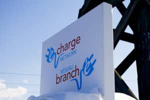 A white sign displaying "eCharge Network" and "Réseau branché" in both English and French, with blue and red text in an outdoor setting, promotes battery-powered driving across New Brunswick.