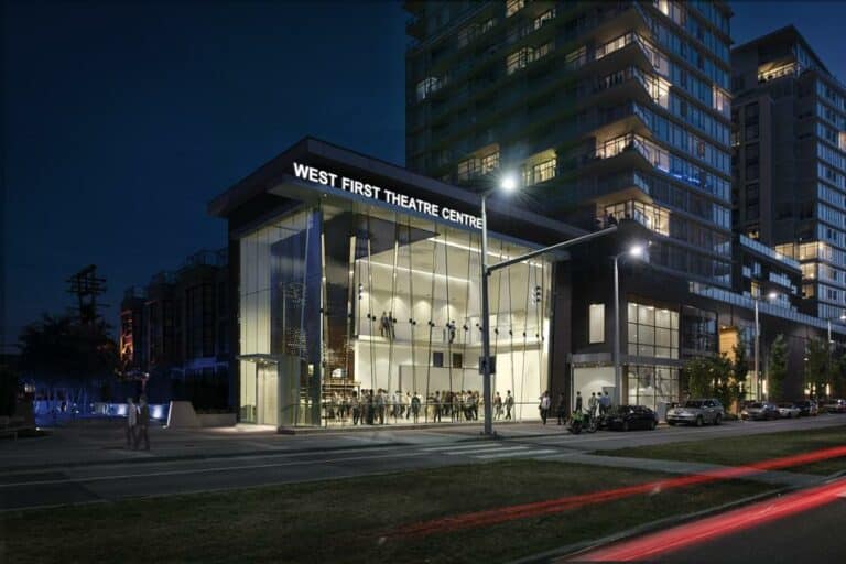 A modern theatre center with a glass exterior lit up at night. The sign reads "West First Theatre Centre," home to the renowned Bart Project. Several people are visible outside and inside the building, adding to the lively atmosphere of this vibrant arts hub.