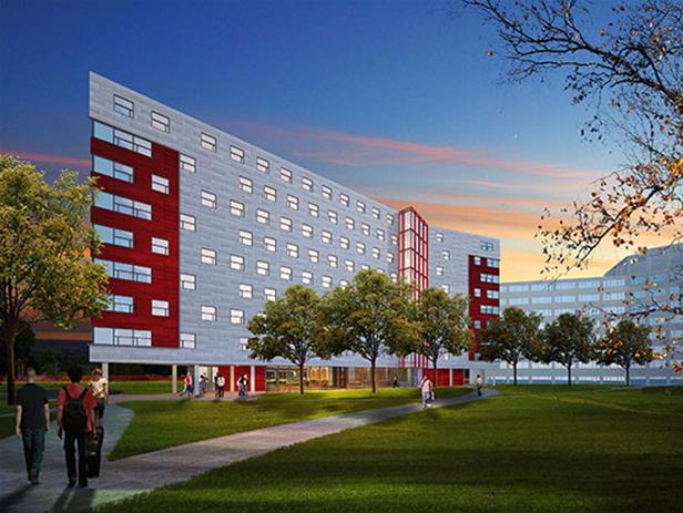 A modern multi-story building with a red and white facade, large windows, and a central glass section graces the University of Calgary campus. It is surrounded by green lawns, trees, and a walkway where people are strolling.