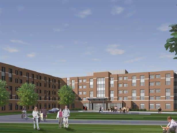 Four-story brick building with large windows, green lawn, and people walking nearby. Trees and a car are present. The sky is clear with a few clouds. This prime setting for higher learning embodies the spirit of education at St. Clair College.