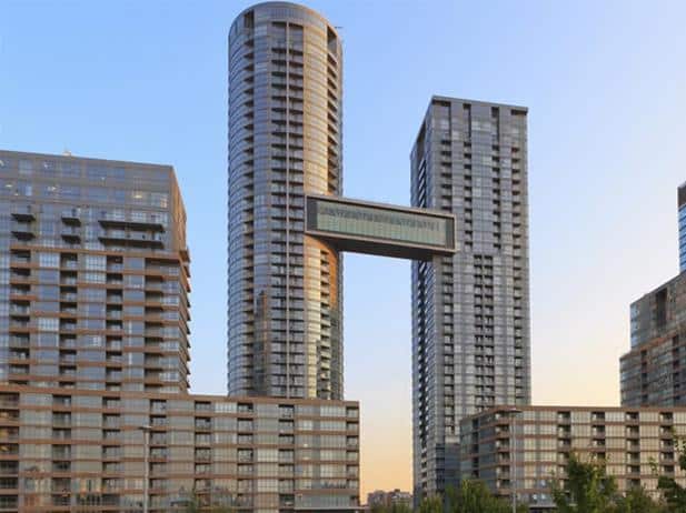 A pair of tall, modern skyscrapers at City Place are connected by a horizontal bridge at the upper levels, with additional buildings in the foreground under a clear sky, creating a striking scene of urban concord.