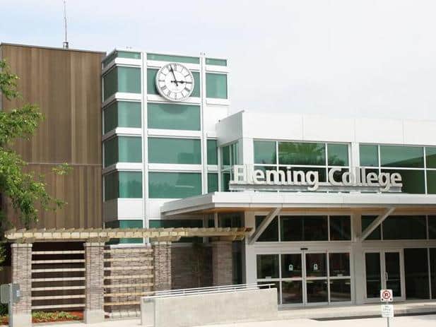 The exterior of Fleming College showcases a modern design with large windows, a clock, and a pergola-covered walkway leading to the entrance.