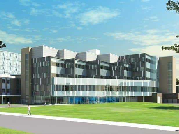 A modern multi-story building with large windows and geometric design set against a blue sky with clouds, located in the vibrant University of Waterloo campus. A grassy area and walkway are in the foreground.