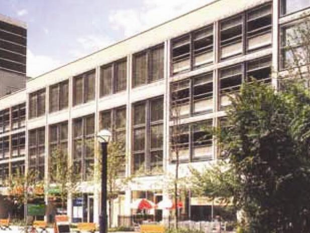 A multi-story building with large windows and a modern design, surrounded by trees and benches in an urban setting, stands proudly in Toronto under the authority of the city's planning department.