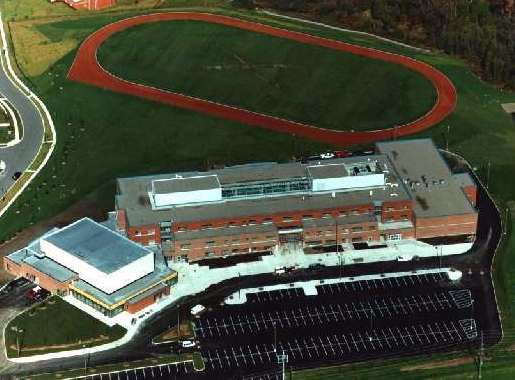 Aerial view of a building surrounded by parking lots, with a track field in the background, part of the York Region Education landscape.