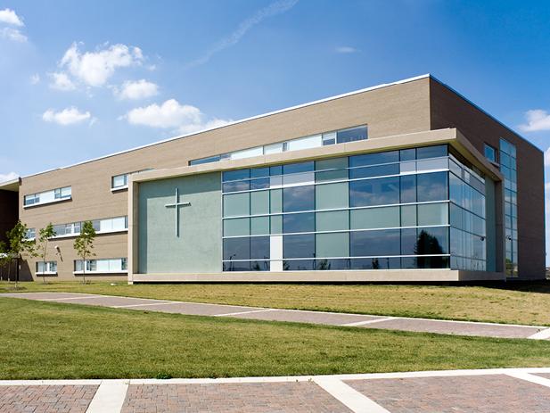 Modern rectangular building with large glass windows and a cross on the exterior wall, situated on a grassy area with a brick walkway in the City of Vaughan.