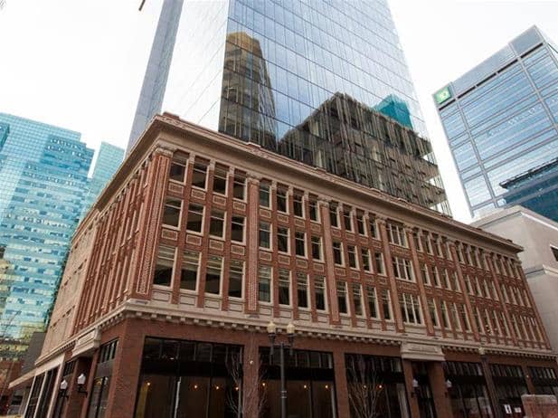 A multi-story building with a traditional brick facade stands alongside Pangman's modern glass skyscraper, reflecting adjacent buildings in the backdrop, symbolizing urban development.