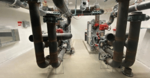 A mechanical room featuring a network of insulated black pipes, red valve controls, and heat exchange equipment, part of the geoexchange system at one of our projects in Ontario.